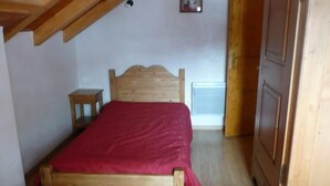 Een houten bed met een rode spreidek, in een kamer met houten wanden en een schuine kap.