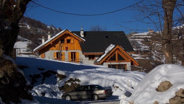 Een houten chalet met een schuin dak, een auto ervoor en een besneeuwde omgeving.