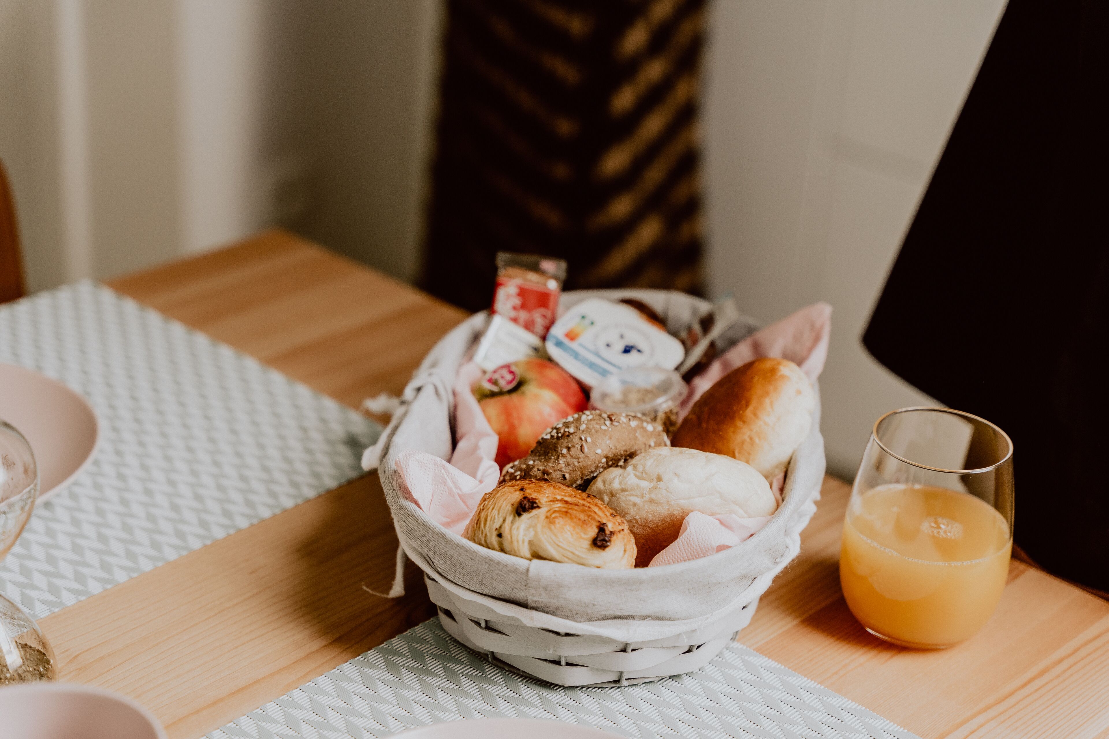 A basket of assorted pastries and a glass of orange juice on a wooden table.