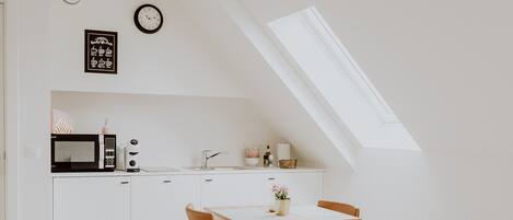 A modern, well-lit living room with a high ceiling, a dining area, and a kitchen.