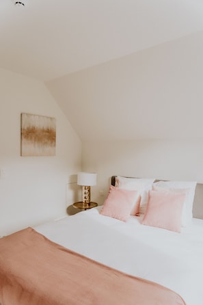 Un dormitorio con cama, mesita de noche, lámpara y un cuadro colgado en la pared.
