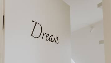 A door with the word "Dream" on it, leading into a room with a bed, a table, and a plant.