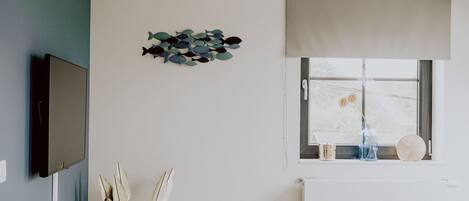 Un soggiorno moderno con una televisione a schermo piatto, un'opera d'arte a parete a forma di pesce, una finestra con persiana a rullo e un tavolino con una ciotola.