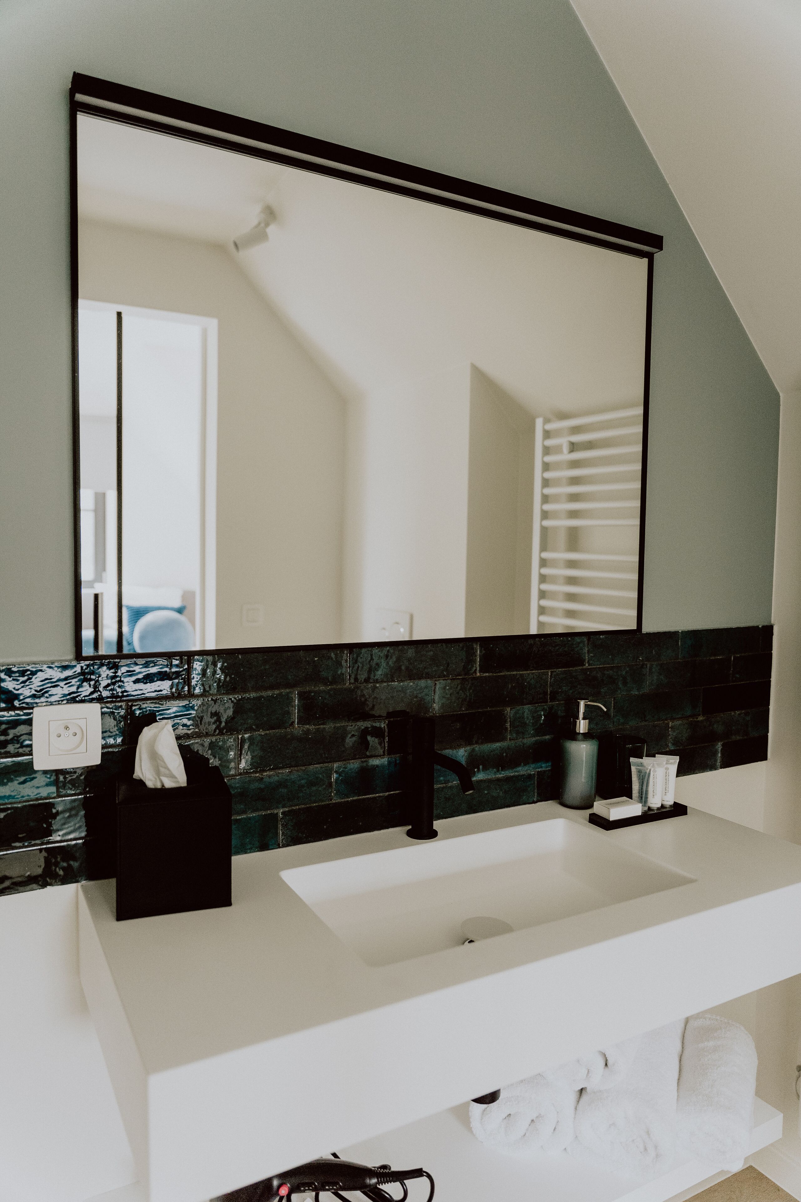 Un baño con lavamanos blanco, grifo negro y un espejo grande encima.