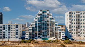 A modern high-rise building with a unique triangular design, featuring multiple balconies and a swimming pool in the center. - Pyramid 11J by Seaside Vacations & Sales (Ocean City)