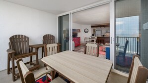 A balcony with a wooden table and chairs, a sliding glass door leading to a kitchen, and a view of the cityscape. - Pyramid 11J by Seaside Vacations & Sales (Ocean City)