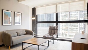 A modern living room with a sofa, a chair, a coffee table, and a large window with blinds.