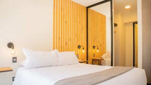 A modern hotel room with a large bed, wooden panel wall, and bedside lamps.