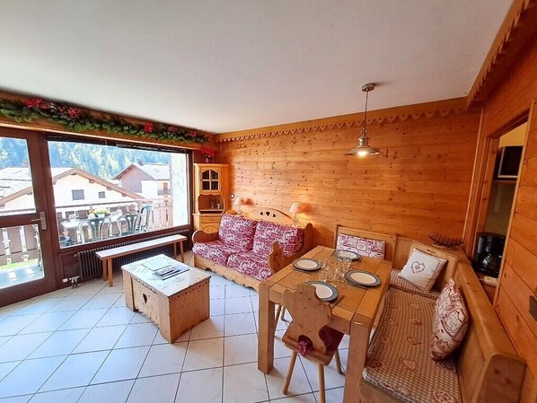 A wooden interior with a dining table set for four, a sofa, and a bench. - Studio with balcony, in the heart of the village (Le Grand-Bornand)