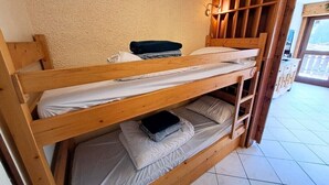 Un lit superposé avec une structure en bois, une literie blanche et un petit objet noir sur le lit du bas.