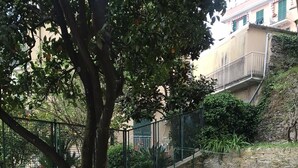 Un patio al aire libre con una mesa lista para comer, rodeado de sillas, un árbol y una pared de piedra.