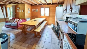 Ein gemütliches Blockhaus mit Holzvertäfelung, einem Esstisch, einer Couch und einer Küchenzeile.