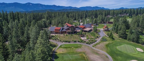 An aerial view of a lodge with multiple buildings, surrounded by dense forest and mountains.