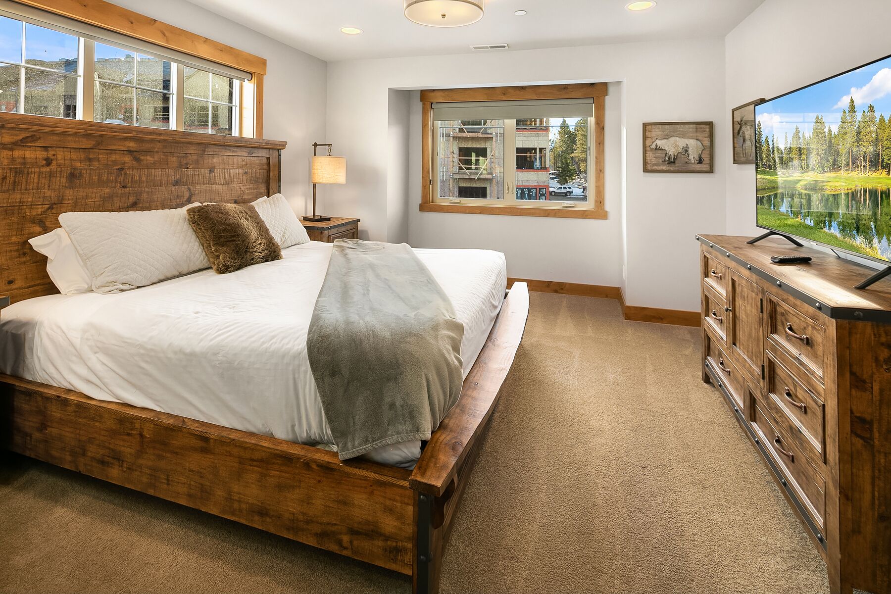 A bedroom with a wooden bed, a TV, and a window with a view of trees and a lake.