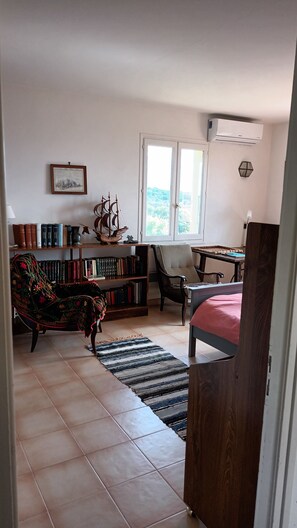 A room with a bed, a desk, a chair, a bookshelf, and a window with a view of trees.