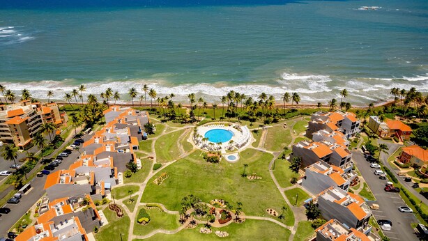An aerial view of a resort with a central pool, beachfront villas, and a view of the ocean. - Rooftop Views, Private Beach Path & Resort Living in Palmas Del Mar (Humacao)