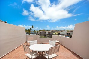 Une table ronde entourée de quatre chaises, sur un balcon offrant une vue sur des palmiers et des immeubles.