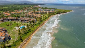An aerial view of a coastal resort with multiple buildings, a beachfront, and a swimming pool. - Rooftop Views, Private Beach Path & Resort Living in Palmas Del Mar (Humacao)