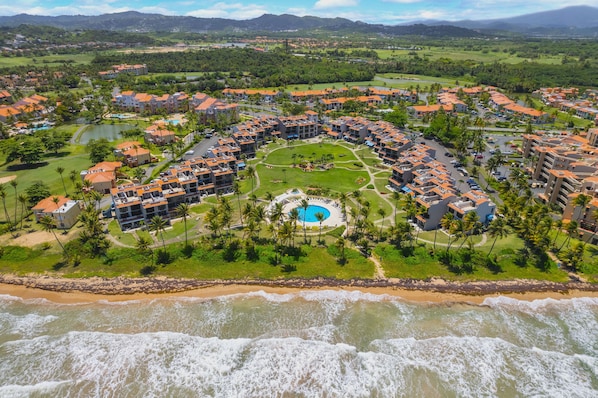 Vue aérienne d’un complexe hôtelier doté d’une piscine circulaire, d’une plage et de plusieurs bâtiments aux toits orange.