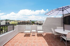Une terrasse avec une table et des chaises, un parasol à rayures et une vue sur les bâtiments en arrière-plan.