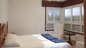 A bedroom with a bed, a chair, a small table, and a window with blinds. - Beachfront property (Malpica)