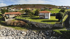 A coastal property with a stone wall, a grassy lawn, and a small building with a red roof. - Beachfront property (Malpica)
