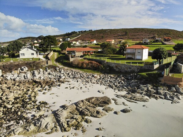Una zona costera con playa pedregosa, un muro de piedra y casas con tejados rojos.