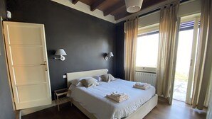 A bedroom with a large bed, two bedside lamps, a wooden floor, a white door, and a window with curtains.