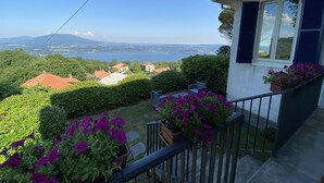 A balcony with potted flowers, a clear view of a lake, and houses in the background.