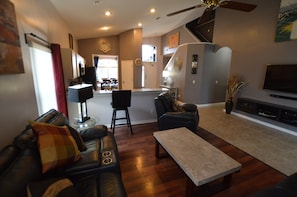 A modern living room with a leather sofa, a coffee table, and a TV. There is a staircase leading to an upper level.