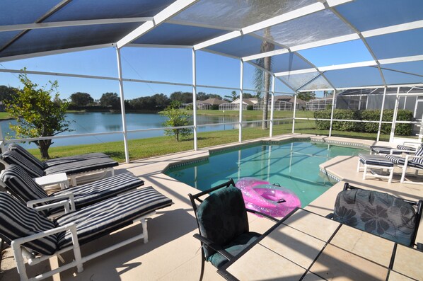 A covered outdoor pool area with lounge chairs and a view of a lake.