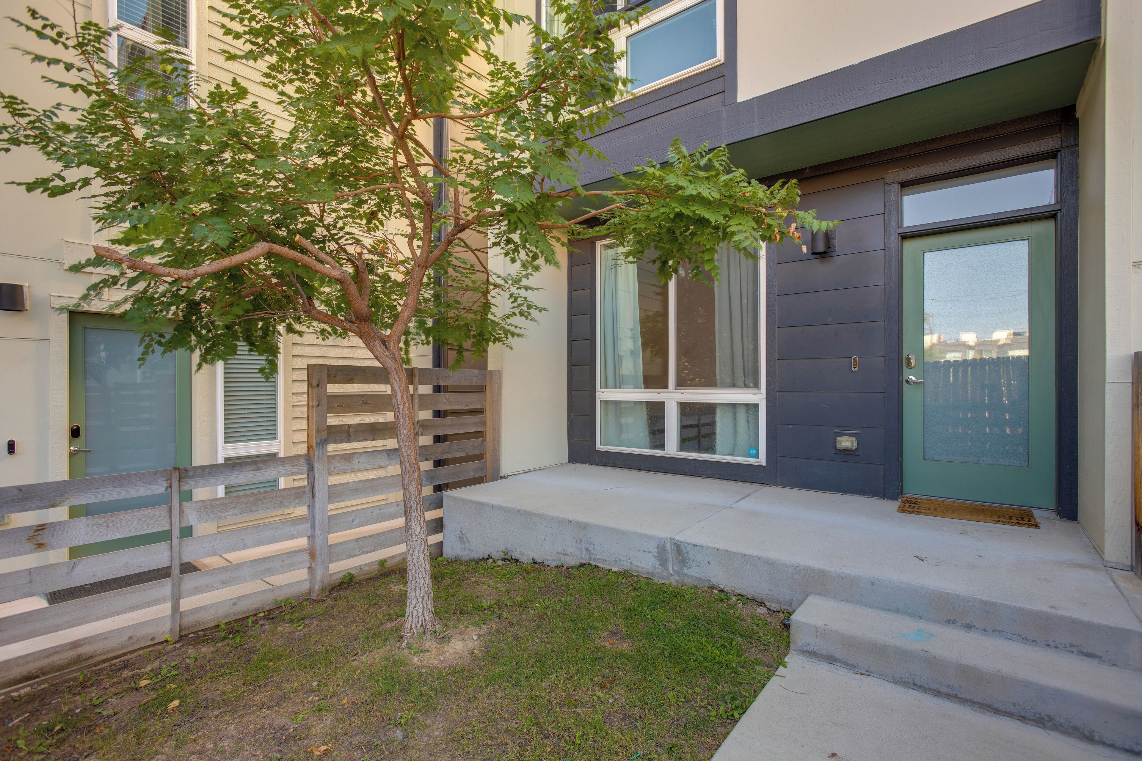 A modern two-story house with a front door, a small tree, and a wooden fence.