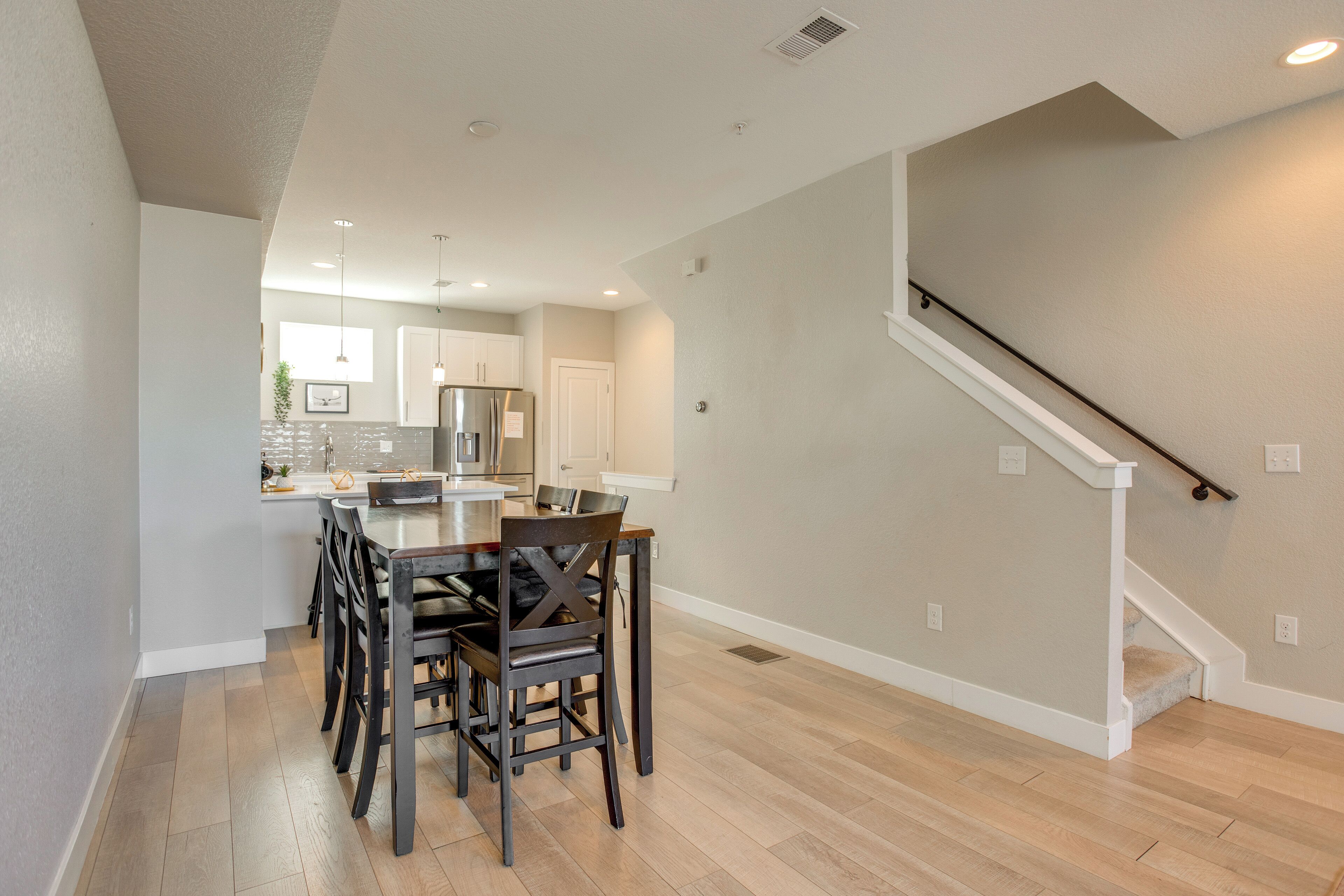 A modern kitchen with white cabinets, a dining table with chairs, and a staircase with a white railing.