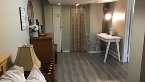 A hotel room with a bed, a desk, a chair, a mirror, and a bathroom with a shower curtain.