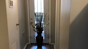 A hallway with a door at the end, a potted plant in the center, and a vent on the left wall.