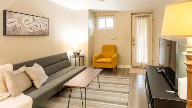 A living room with a sofa, a small table, a yellow armchair, a TV, and a painting on the wall.