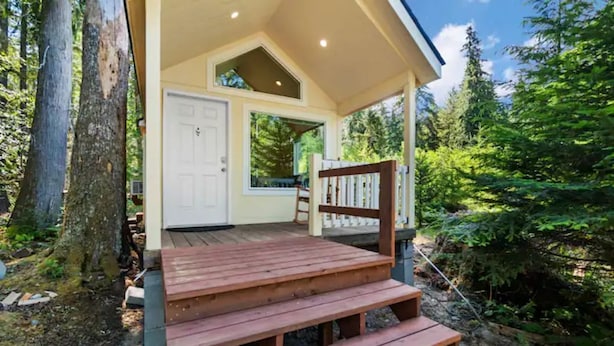 Une terrasse en bois mène à un porche abrité, doté d’une porte blanche et d’une petite fenêtre.