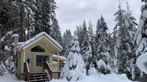 Une cabane enneigée avec une véranda et des marches menant à l’entrée.