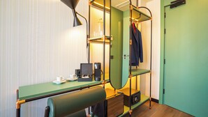 Una habitación de hotel compacta con escritorio verde, espejo, perchero y puerta verde.