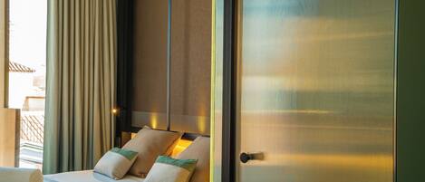 A hotel room with a large bed, a view through a window, and a door with a metal handle.