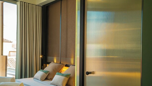 Una habitación de hotel con una cama grande, vistas por una ventana y una puerta con manija de metal.