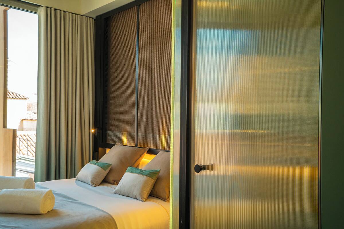 A hotel room with a large bed, a view through a window, and a door with a metal handle.