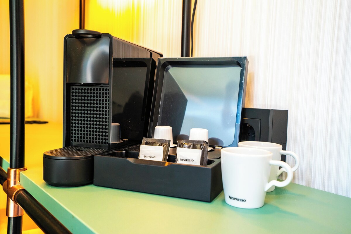 A coffee machine with a tray of coffee pods and two white mugs on a green surface.
