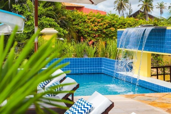 A pool with a waterfall feature, surrounded by lush greenery and a tiled poolside. - Aimberê Eco Resort Hotel (Luis Correia)