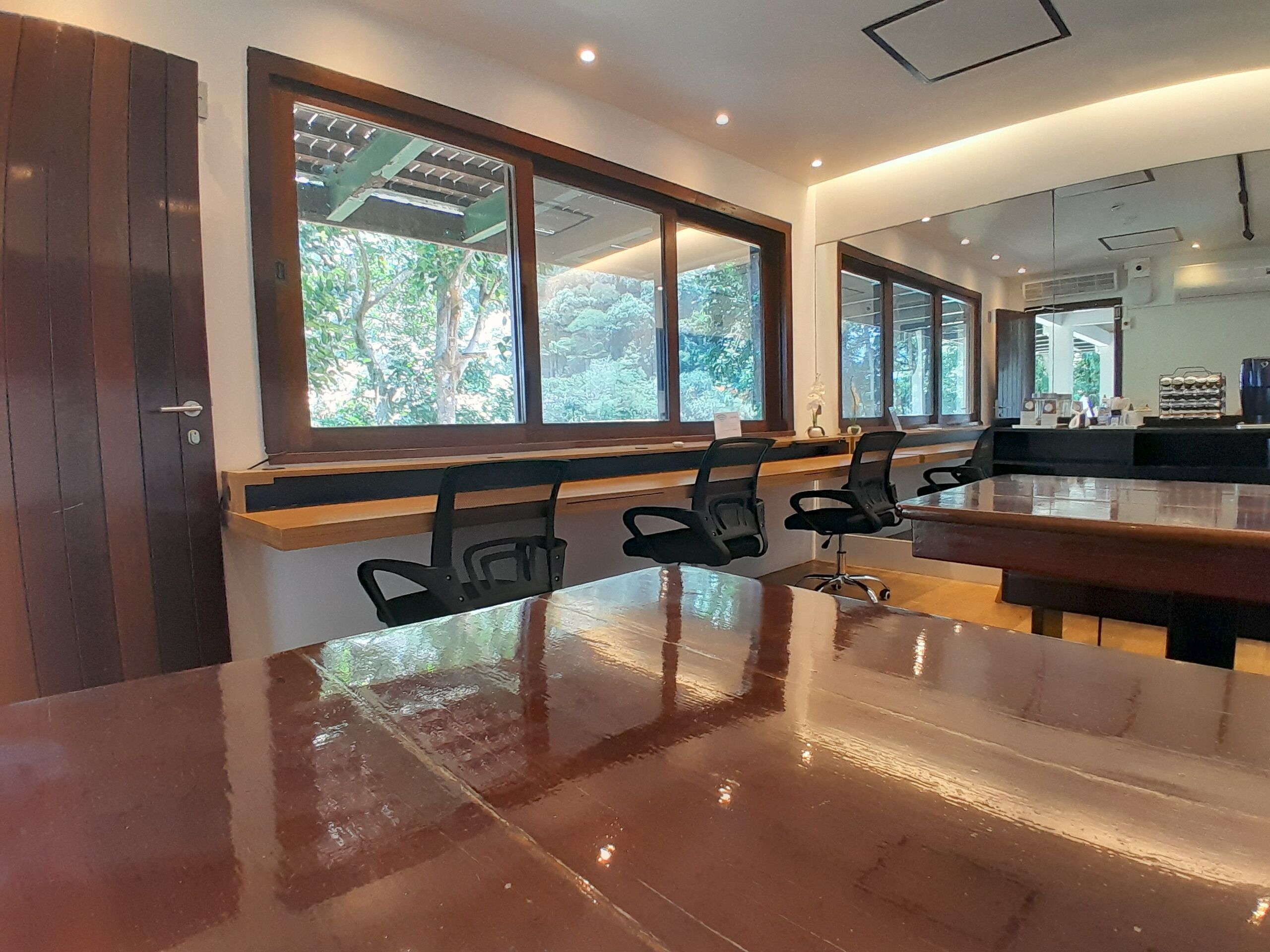 A conference room with a long table, several chairs, and large windows offering a view of greenery outside.