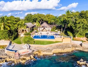 A large house with a swimming pool surrounded by lush greenery and a rocky coastline. - Balinese style villa in seaside in, Dominican Republic (Casa de Campo)