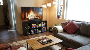 A cozy living room with a fireplace, a television, a bookshelf, and a chessboard on a coffee table. - Blue Mountain Cabin Escape/AC/Pet Friendly (Flagstaff)