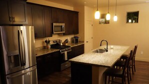 A modern kitchen with dark wood cabinets, stainless steel appliances, granite countertops, and pendant lighting. - Blue Mountain Cabin Escape/AC/Pet Friendly (Flagstaff)