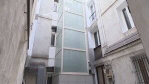 A narrow alleyway between buildings with a modern glass and concrete facade, a visible door, and a tiled floor.