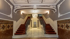A grand staircase with ornate railings and a chandelier, leading to a door at the top.